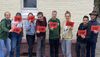 Gruppe von acht Jugendlichen steht vor einer Hauswand und hält jeweils ein rotes Schild mit der Aufschrift 'STOP'.
