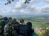 Das Bild zeigt eine Gruppe Jugendlicher, die einen atemberaubenden Blick hinunter auf die Schwäbische Landschaft genießen. Sie hocken auf einem Felsen am Albtrauff der Schwäbischen Alb. Sie haben große Wanderrucksäcke. Es ist sonnig und man kann viele Kilometer weit blicken.